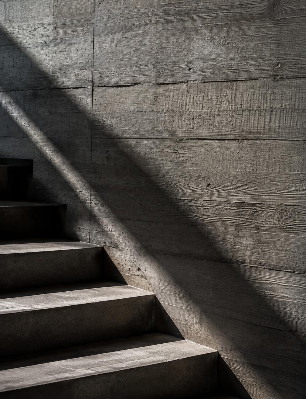 Light falling across a board-formed concrete wall and stairs